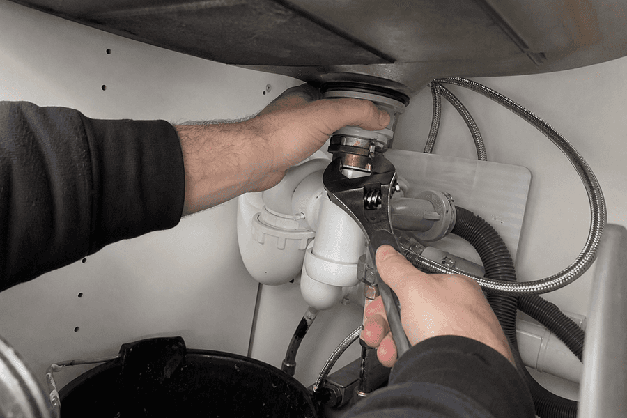 plombier qui resserre un raccord sous un évier